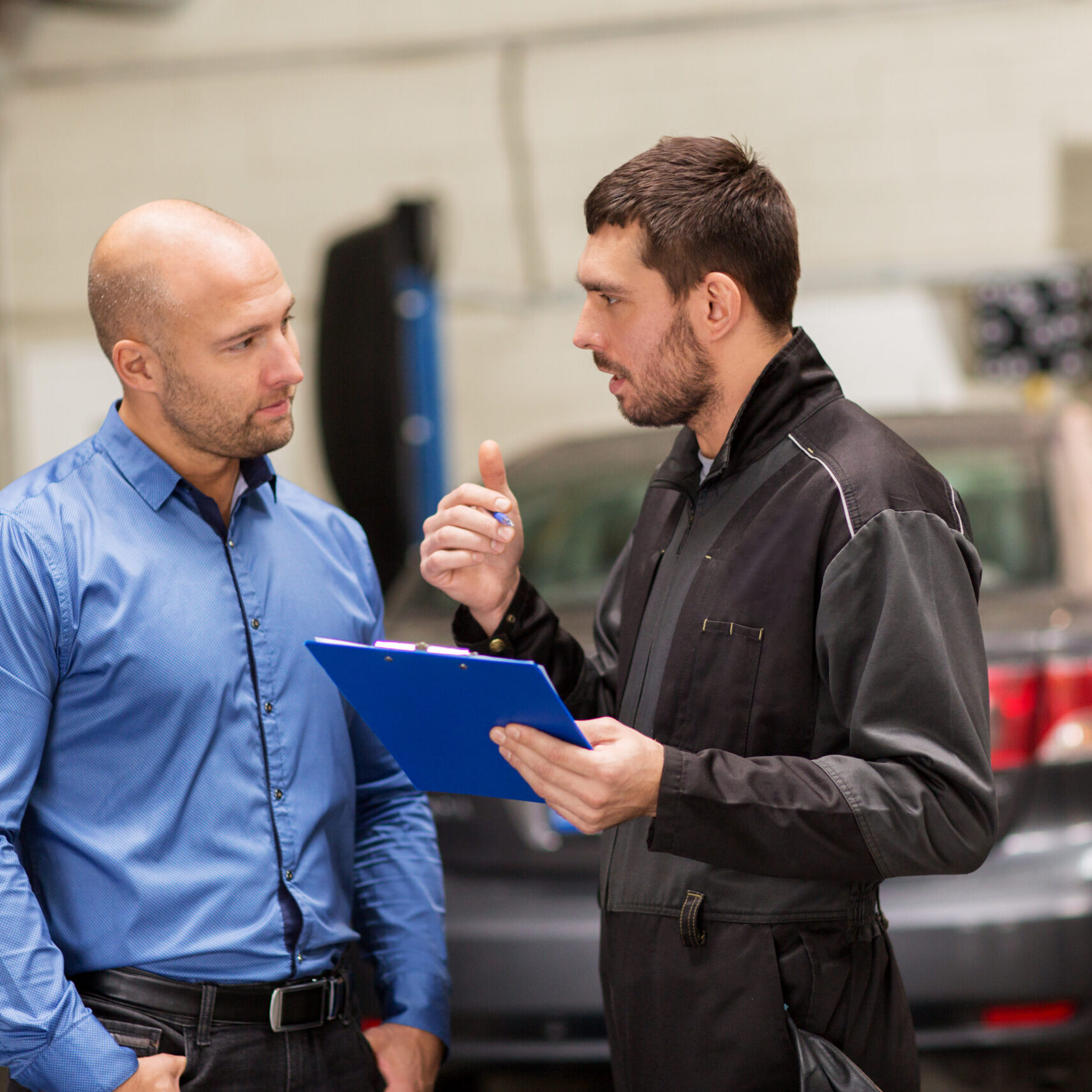 auto mechanic and customer at car shop auto service, repair, maintenance and people concept - mechanic with clipboard and customer or car owner at workshop